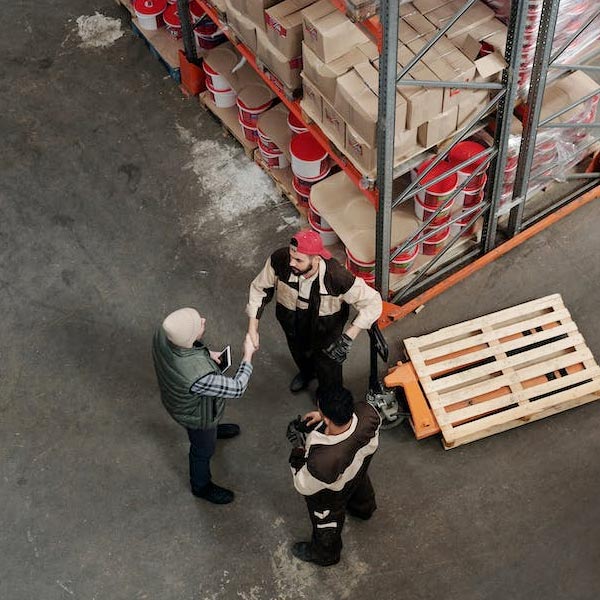 A photo of a birdseye view of three people in a warehouse with jobs at challenge-trg, two of them are shaking hands.