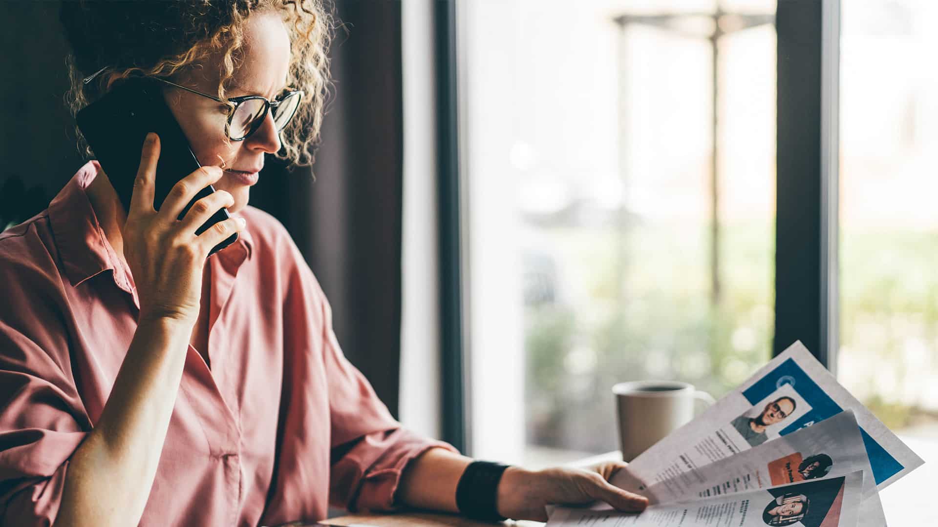 A photo of a woman on the phone holding CV's.