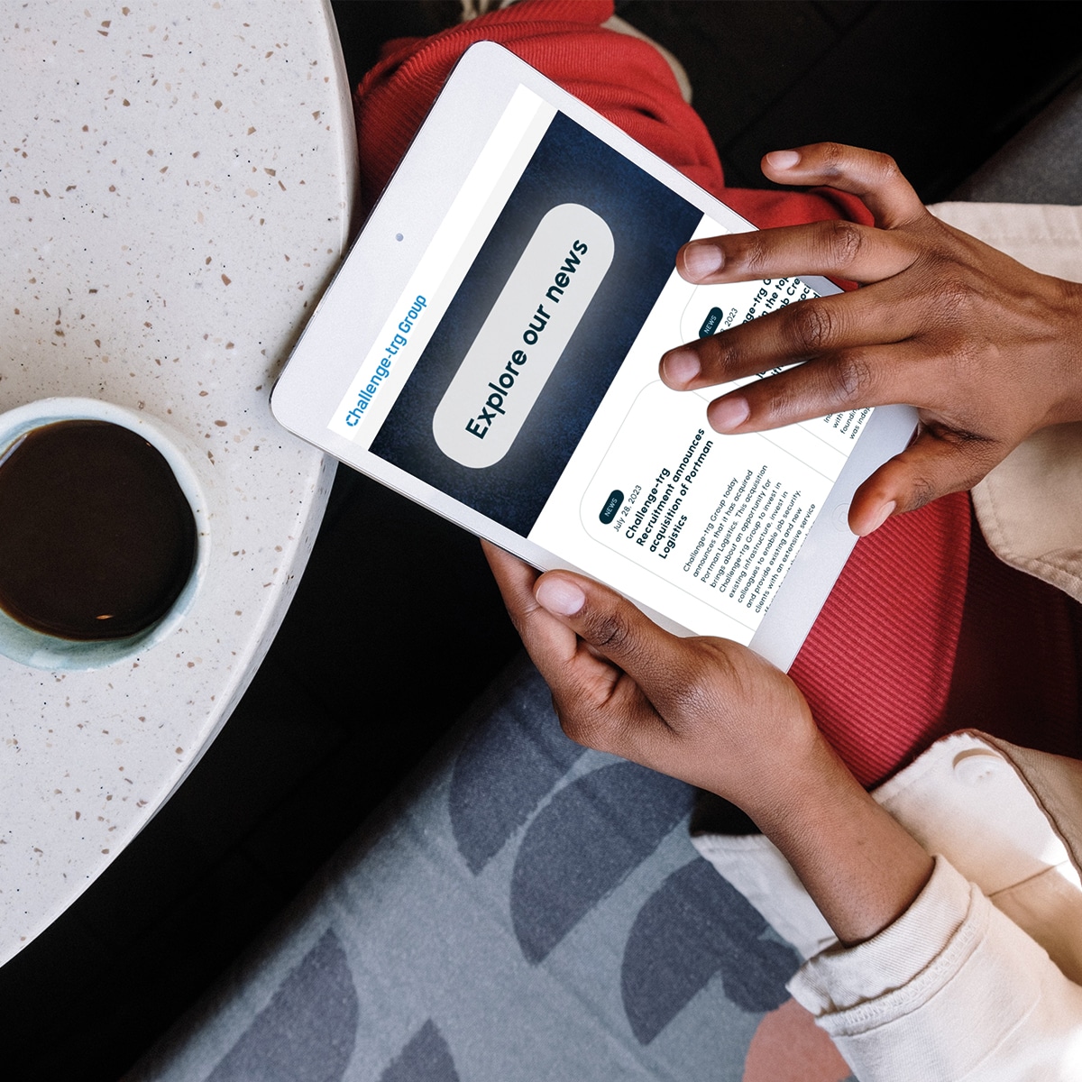 A photo of a hand holding a tablet with the Challenge-trg news page on it.